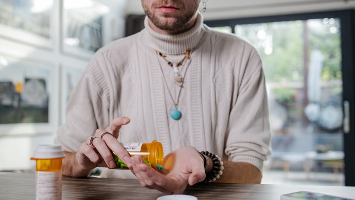 A cropped image of a person pouring pills into their hand.