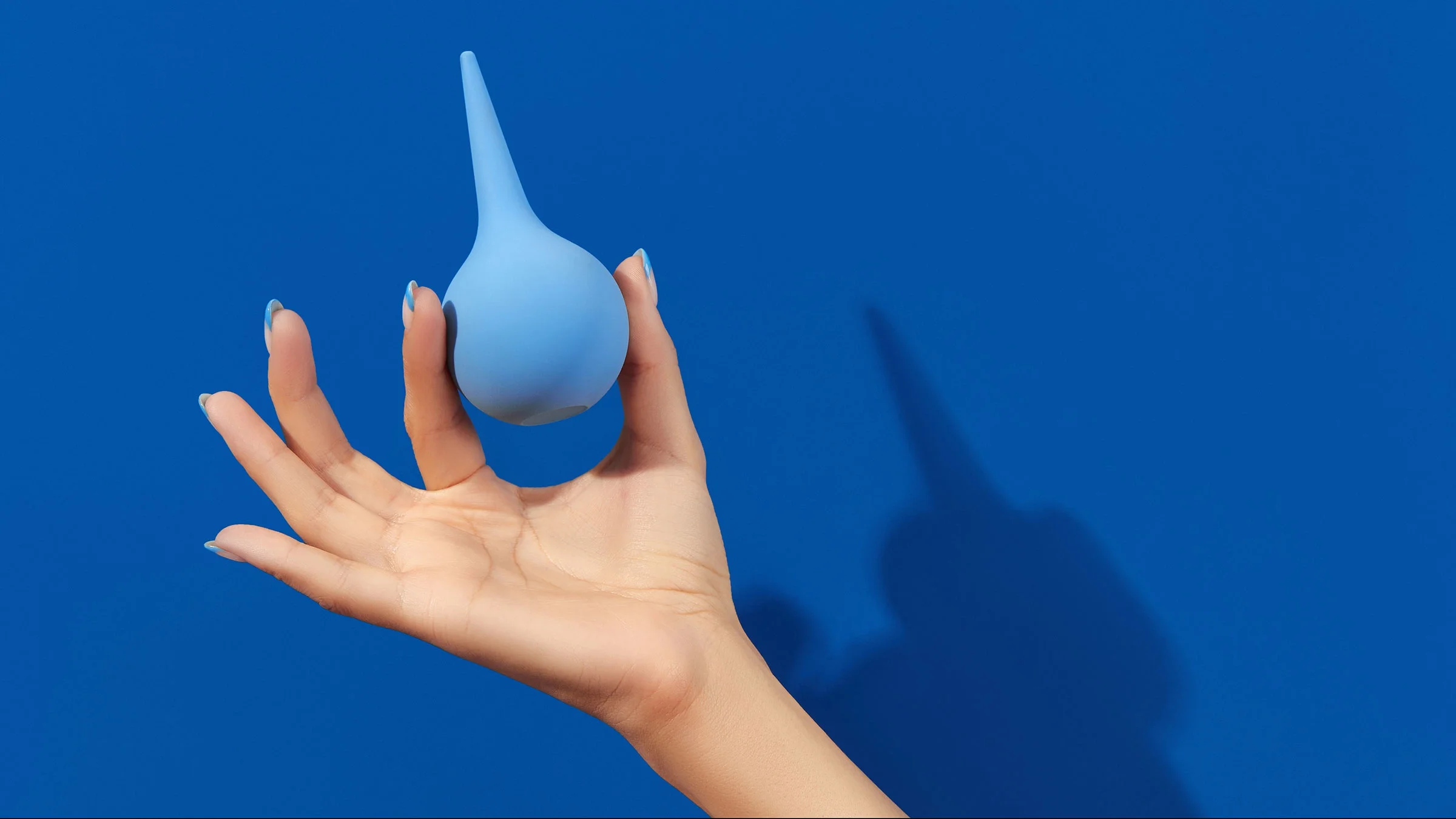 A woman’s hand holds an enema against a blue background.