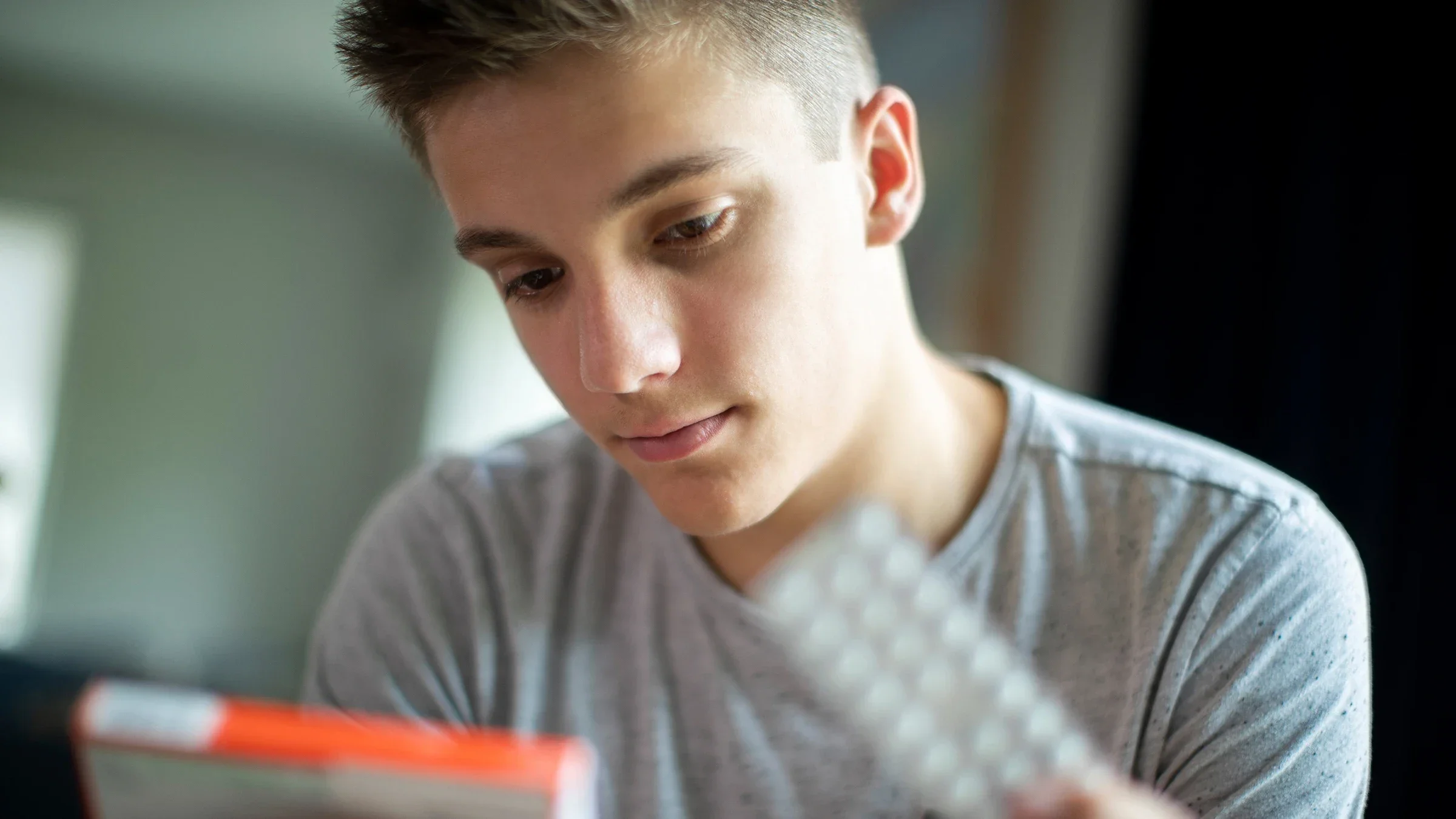 Close-up portrait of a teenage boy opening a package of medication.
Daisy-Daisy/iStock via Getty Images