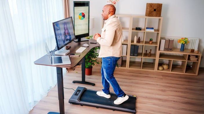 Man using a walking pad under a standing desk during a conference call