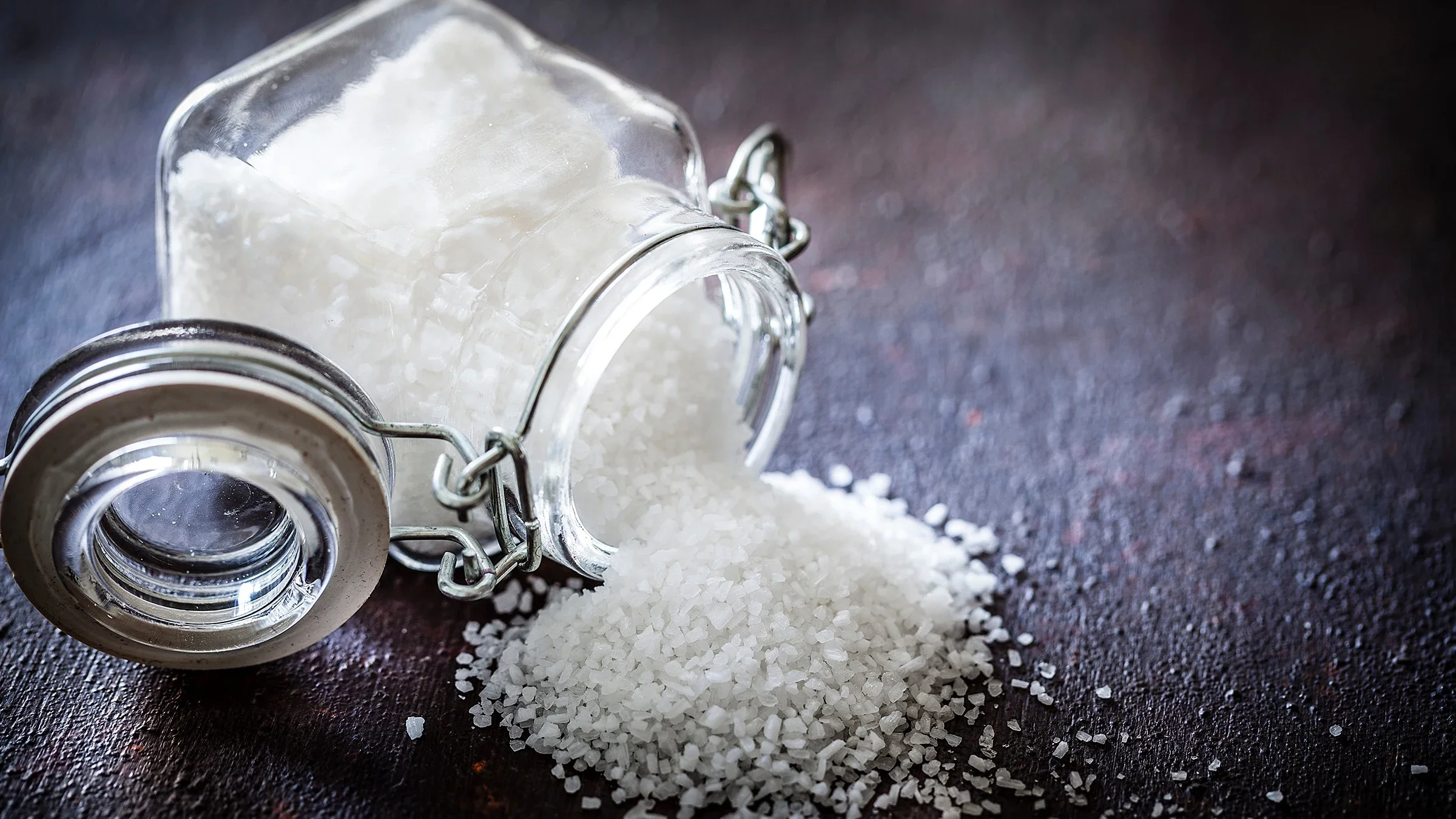Glass jar of corse salt tipped over and spilling onto a textured black background.
fcafotodigital/E+ via Getty Images
