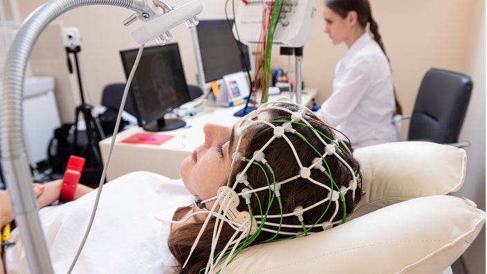 A provider is performing an EEG test on a young woman. It’s a net-like wired device placed over the scalp.