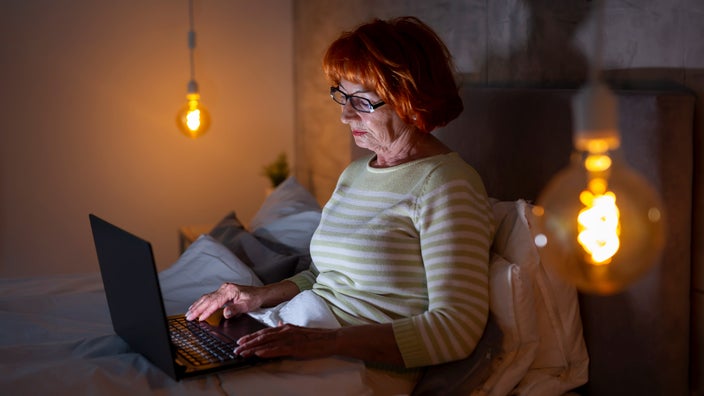 A senior citizen using their laptop in bed.