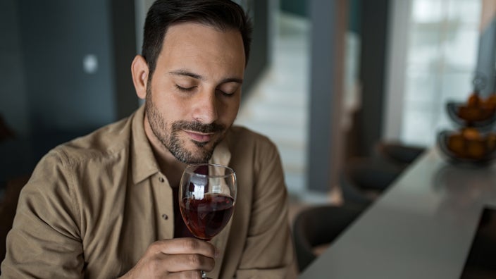A man drinks a glass of red wine at his home. 