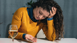 An anxious person holding a pill at a table with a wine glass on it.
Srdjanns74/iStock via Getty Images 