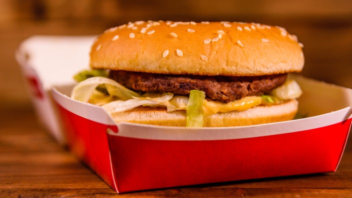 A hamburger in a fast food paper container on a wood table.