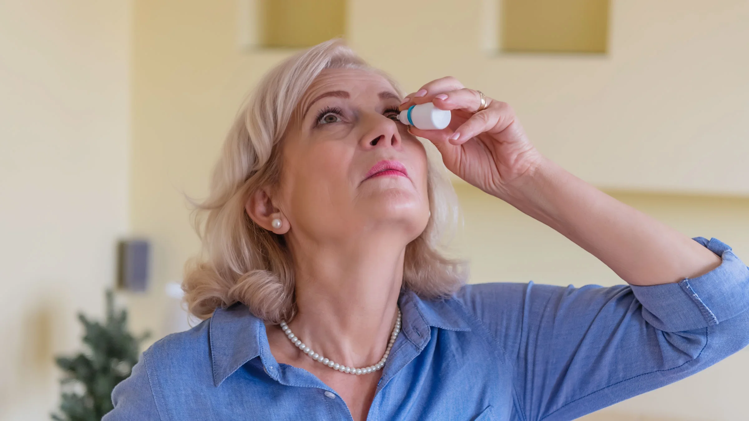 An older woman drops liquid in her eye with an eye-dropper.