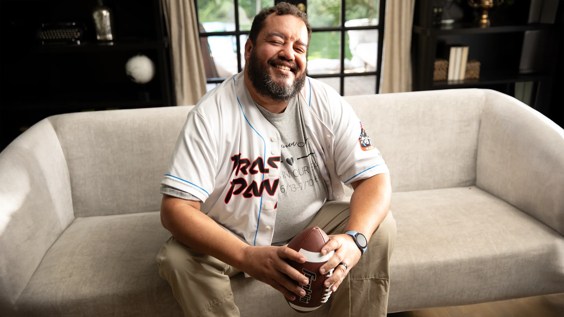 Christopher Lanphere is smiling while holding a football and sitting on a couch.