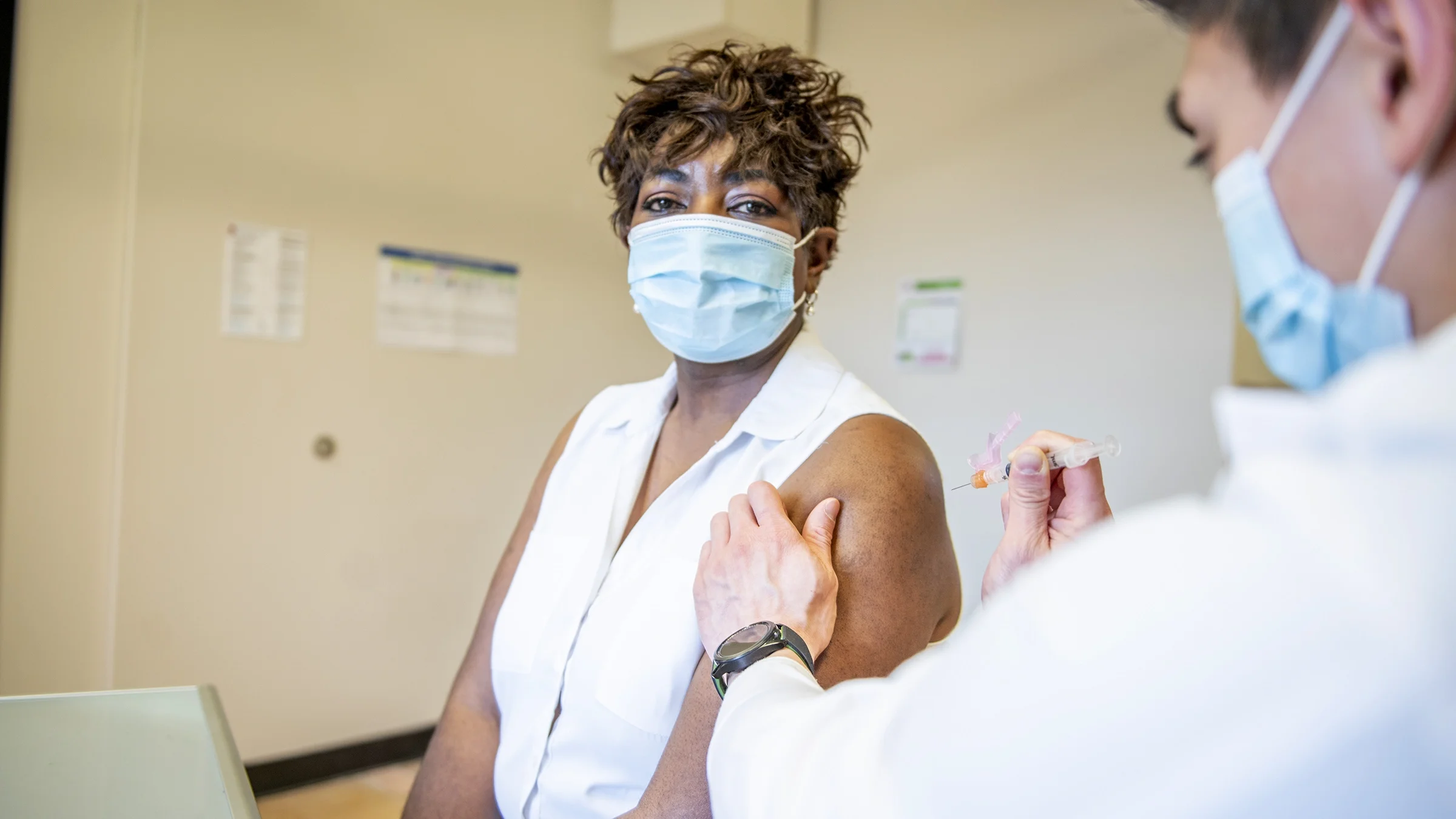 An older woman wearing a face mask getting a shot at the doctor's office.
