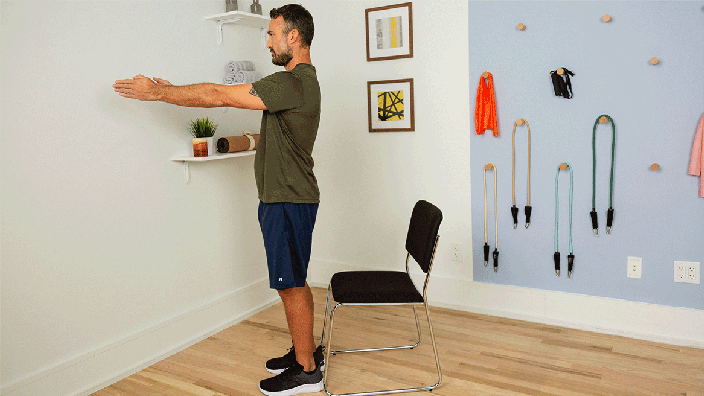 Profile view of man demonstrating squat exercise with a chair behind him.