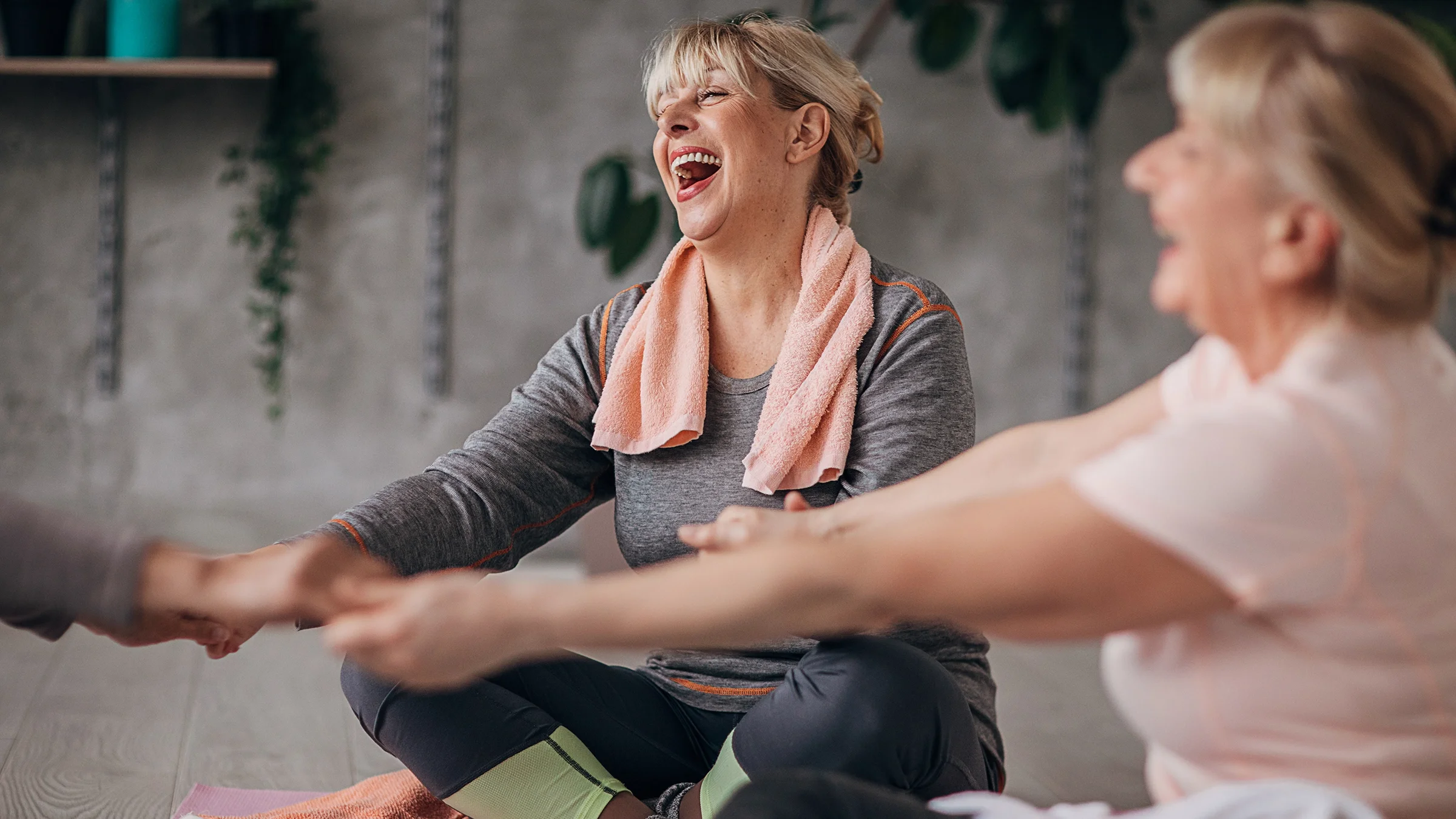 Close-up of women holding hands and laughing in a seated circle at yoga class.