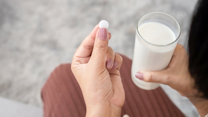 A person holding a pill next to a glass of milk.