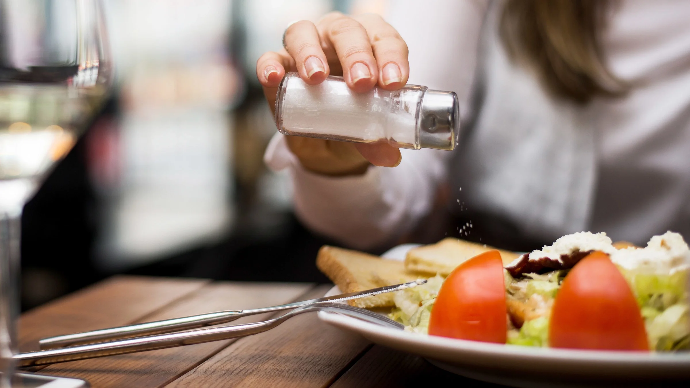 A cropped shot of someone shaking salt onto their restaurant meal.