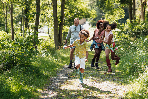 A family running through the trees on a hiking trail–including one man, one woman and two children.