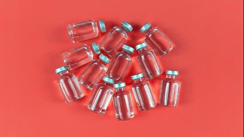 Twelve clear vaccine vials laying on a red background.
