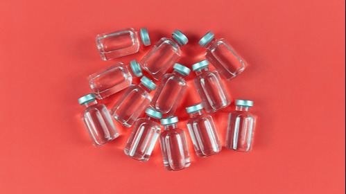 Twelve clear vaccine vials laying on a red background.