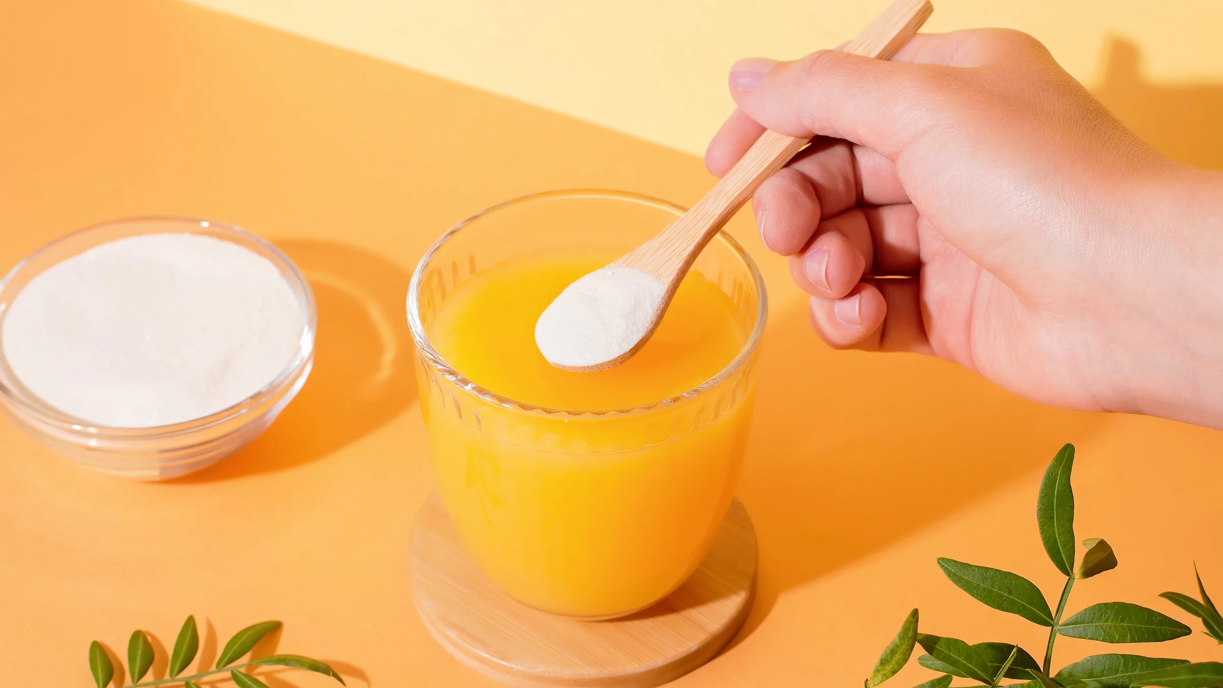 A person is adding collagen powder to orange juice.