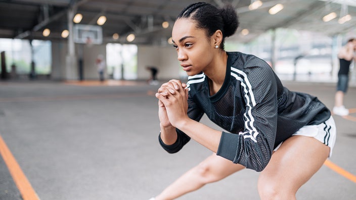 Young woman doing side lunges on a basketball court.