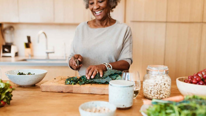 A senior woman is chopping vegetables at her kitchen island.