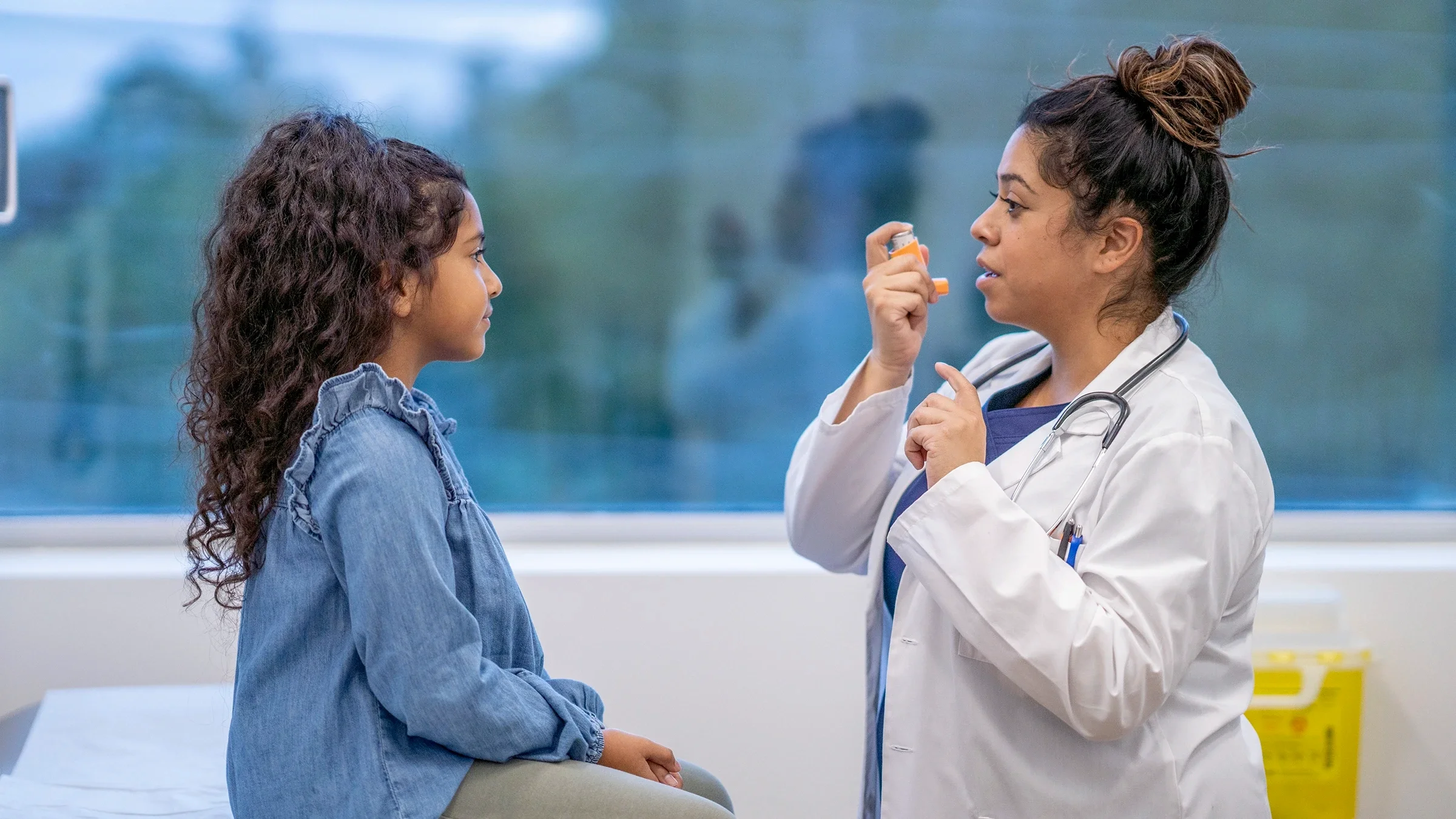 A healthcare practitioner shows a child how to use an inhaler.
