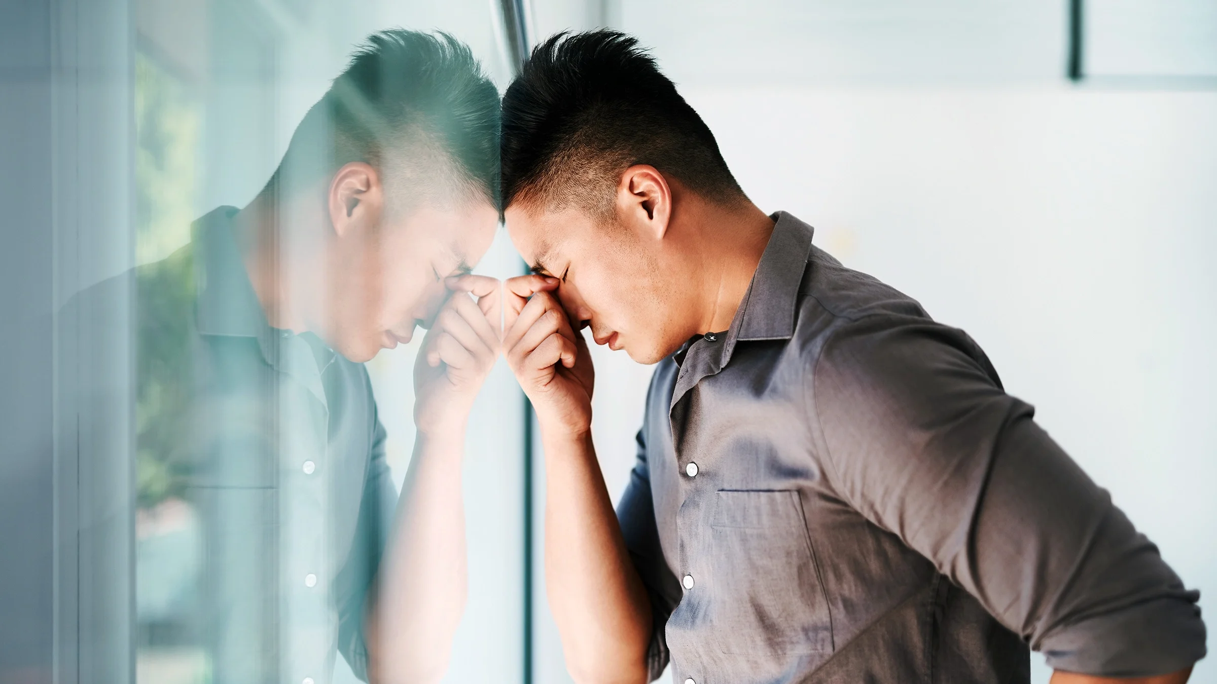 A man is looking stressed out with his head pressed against a window.