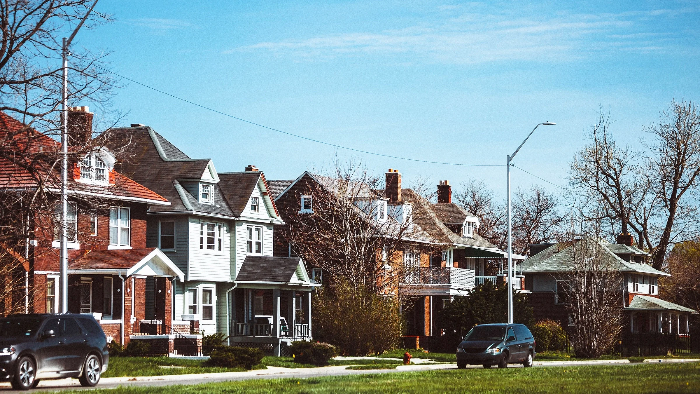 Neighborhood in Detroit with nice two story houses lining the street and a few cars parked out front.