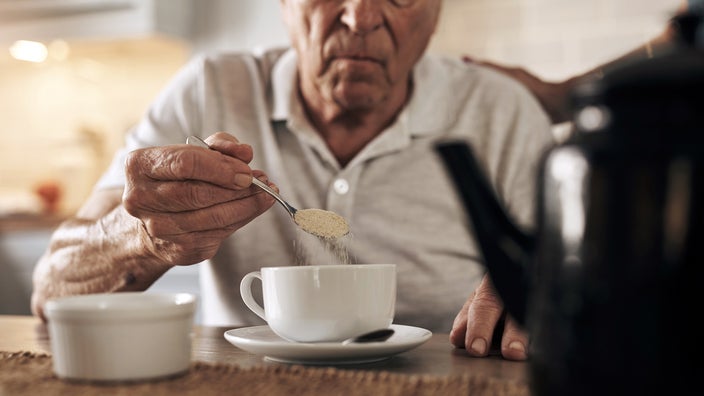 Older man adding sugar to a cup of tea.