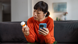 A person holding a pill bottle and a phone.
Maca and Naca/E+ via Getty Images 
