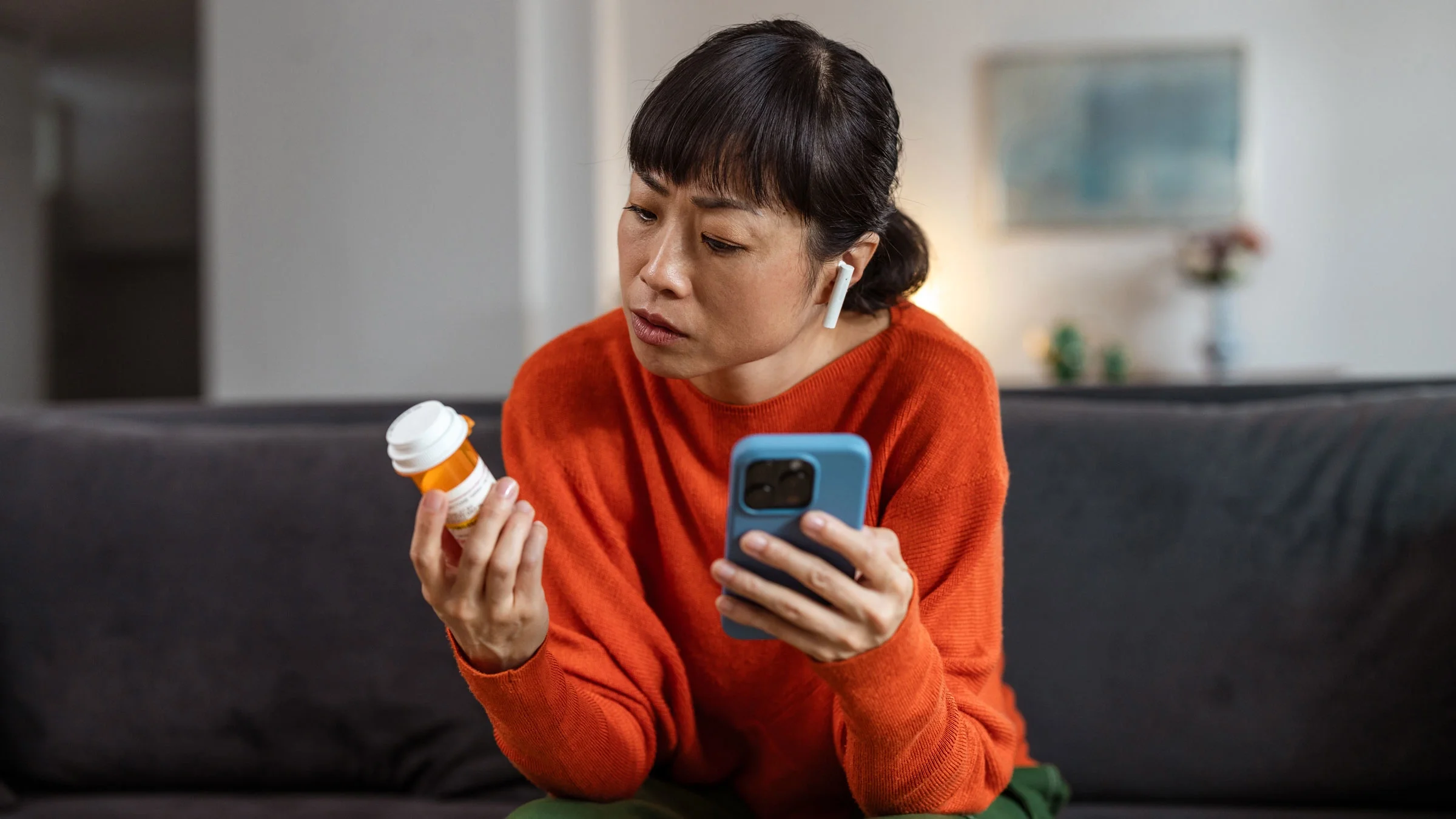 A person holding a pill bottle and a phone.