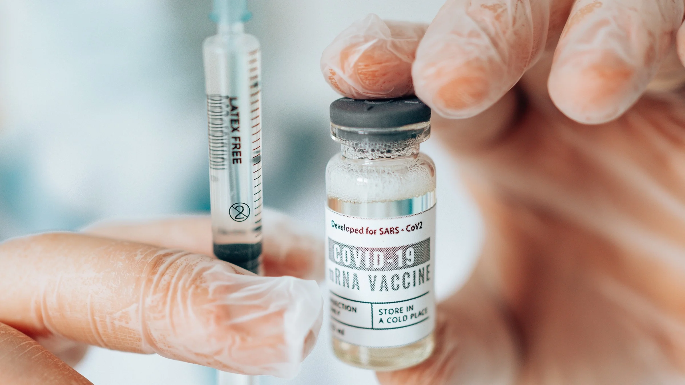 Close-up on a person with clear gloves holding a COVID-19 vaccine vial and syringe.