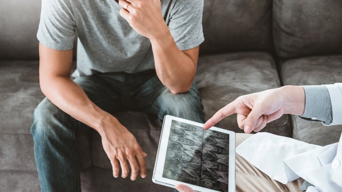 A man going over the images from his CT scan with his doctor. He looks concerned with his hand over his mouth. The doctor is pointing to a part of the scan on the tablet.