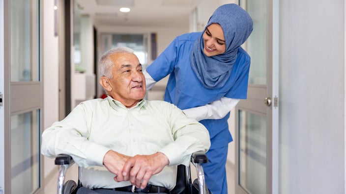 A nurse is accompanying an older patient leaving the hospital in a wheelchair.