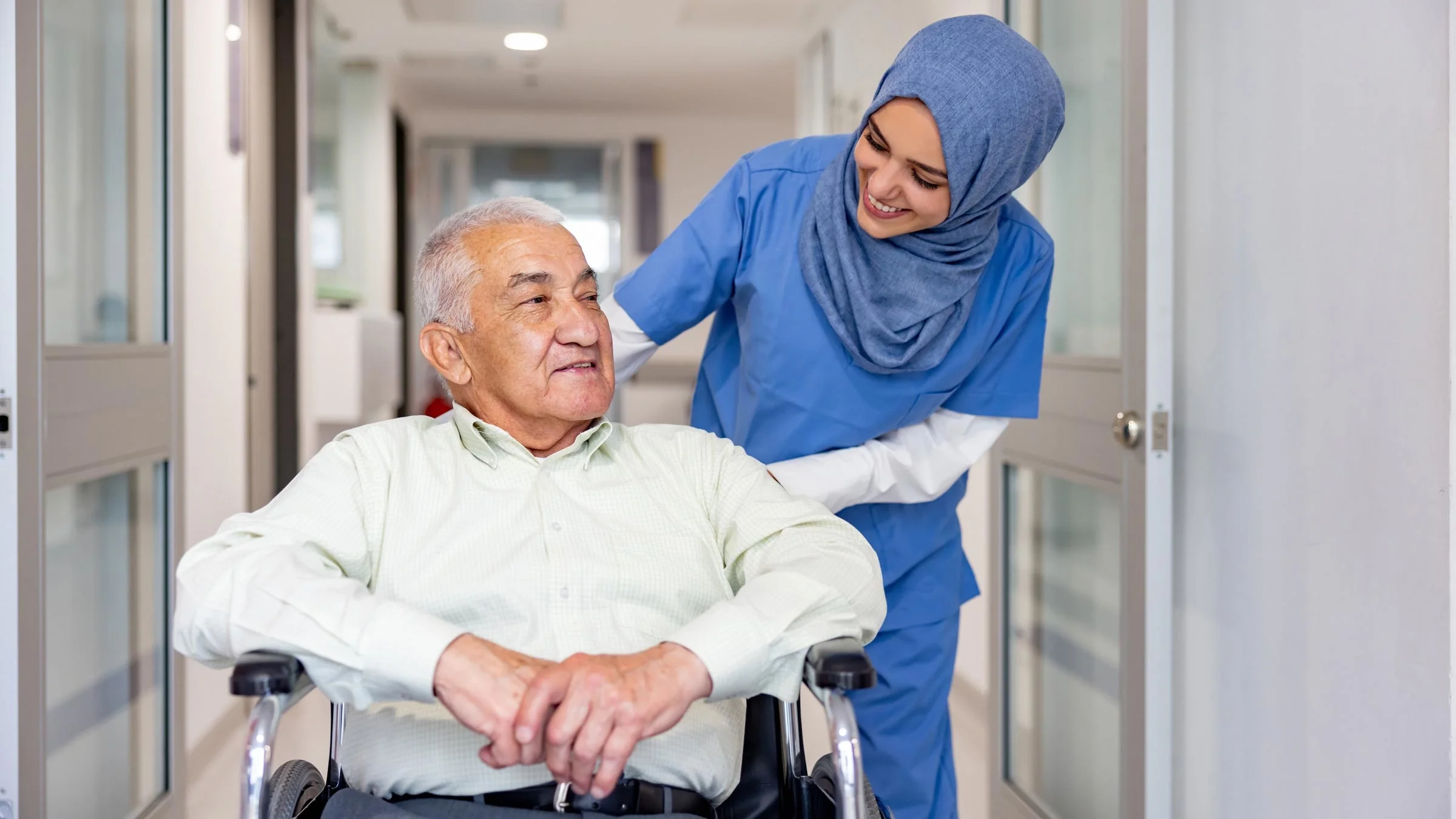 A nurse is accompanying an older patient leaving the hospital in a wheelchair.
