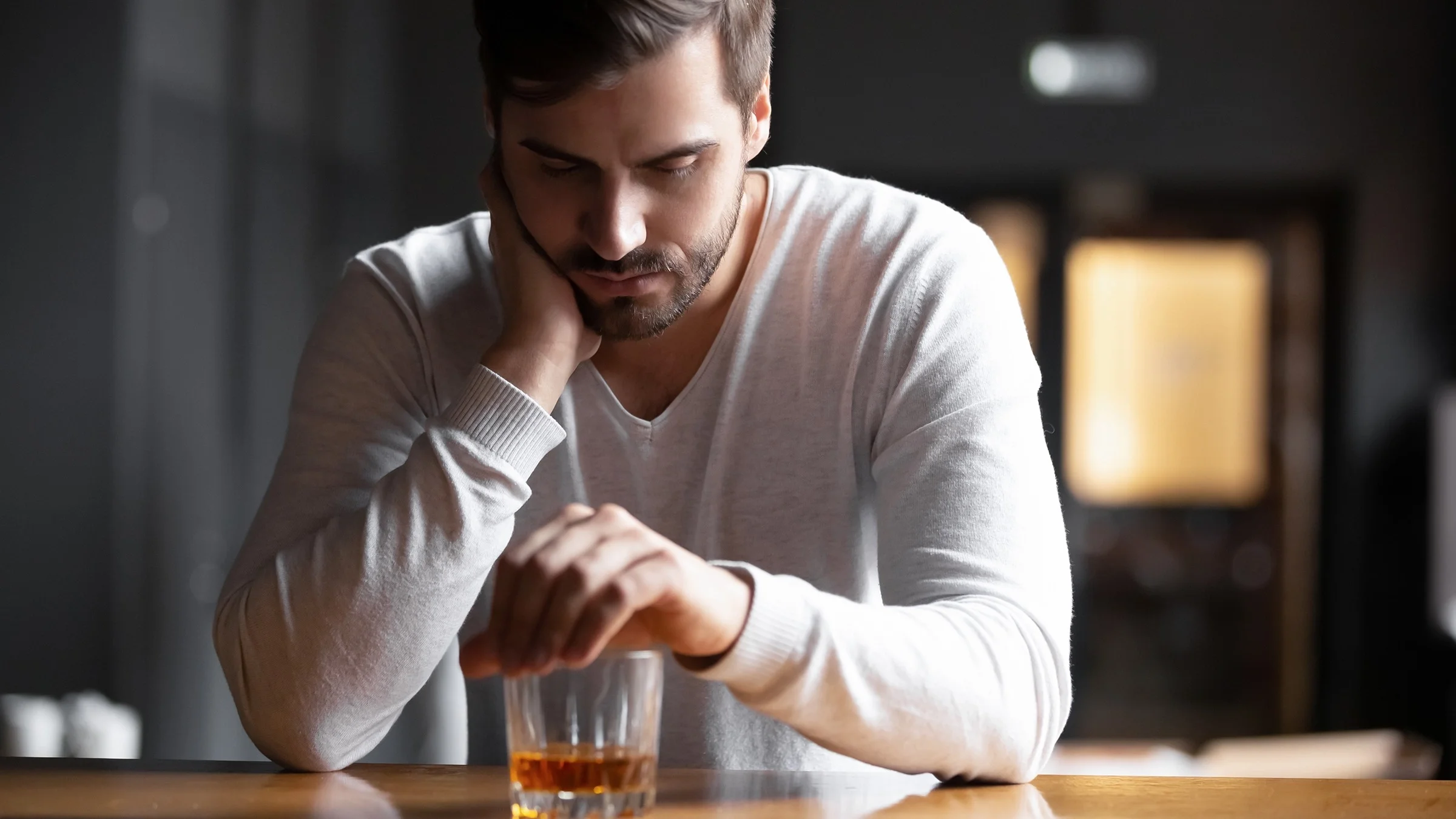 Sad white man with beard drinking a glass of whiskey by himself.