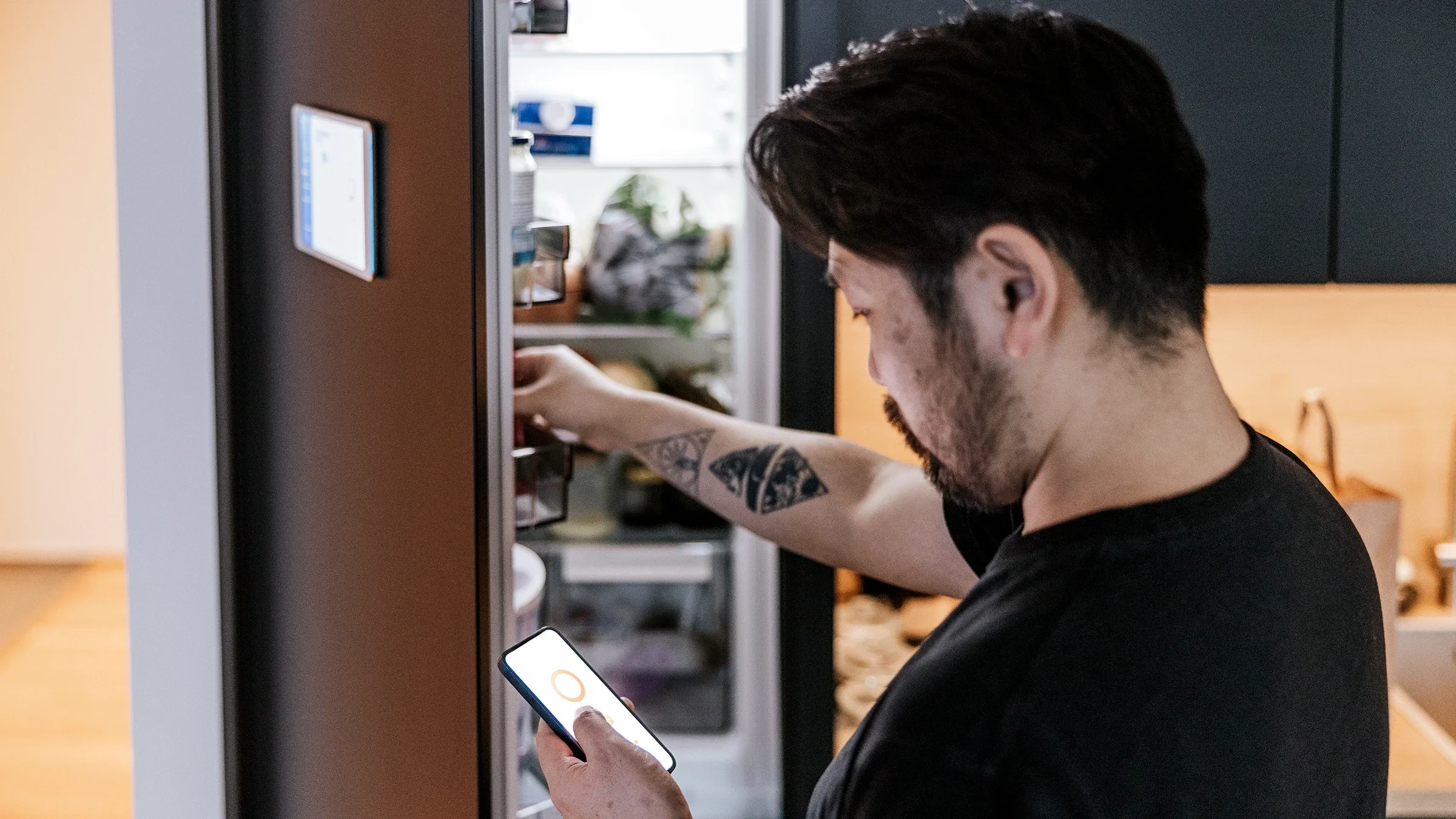 Man opening his fridge and using a smartphone.