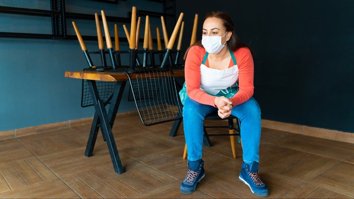 Restaurant worker sitting at an empty table with the chairs up during pandemic times.