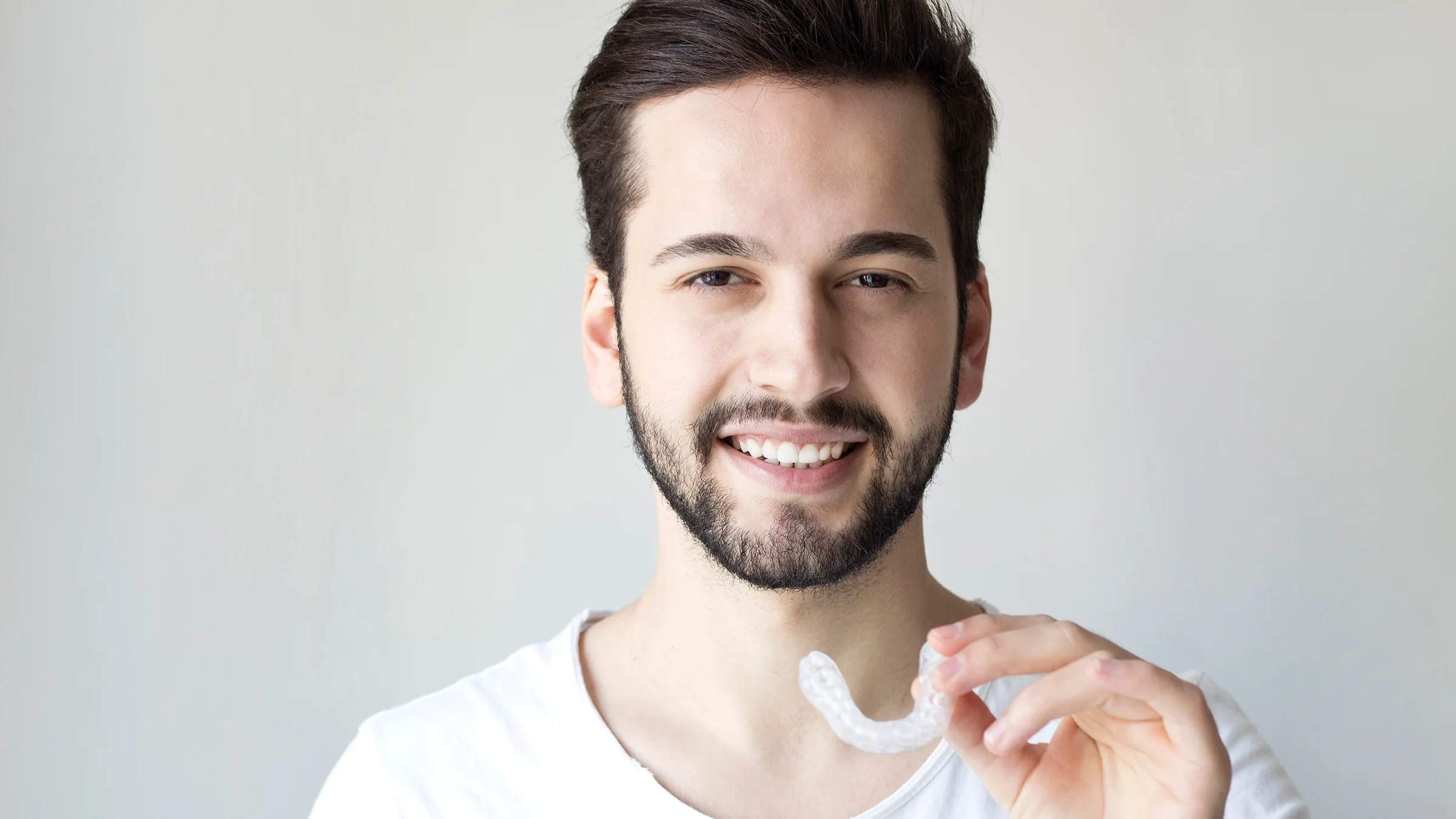 Portrait of a man holding up his night guard to the camera on a plain white background.