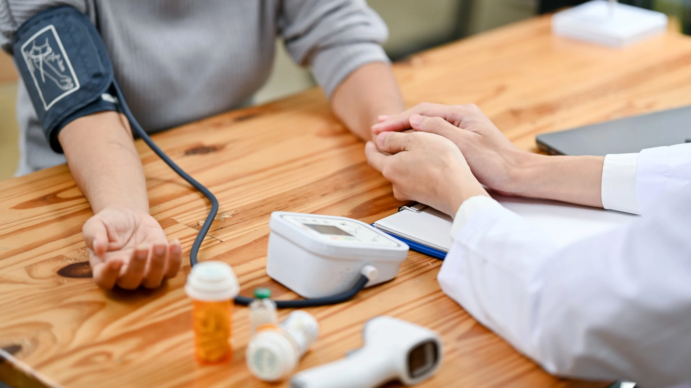 A doctor holding a patient's hand, while taking blood pressure. 