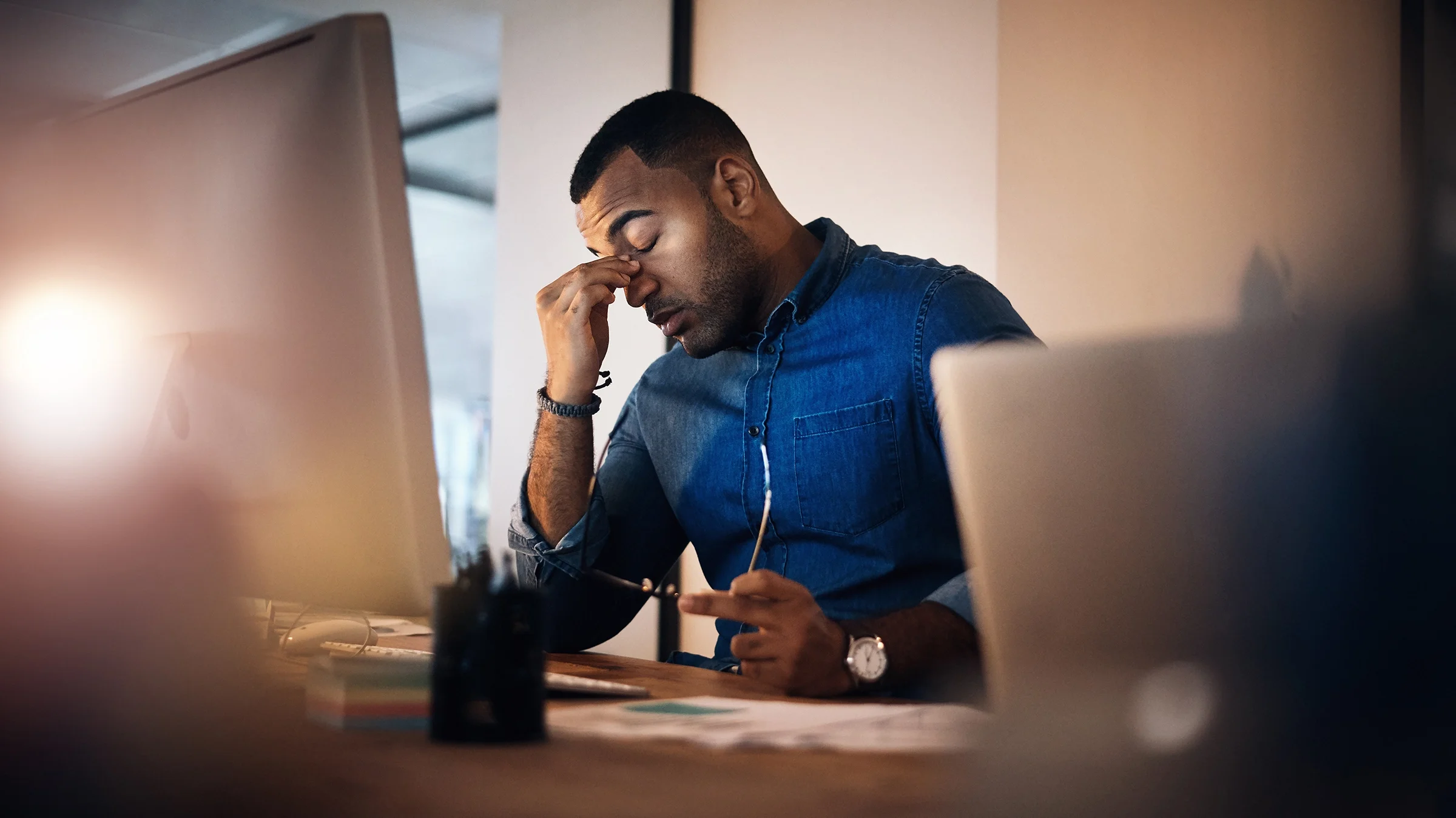 A man who looks like he’s having a migraine is working at his desk.