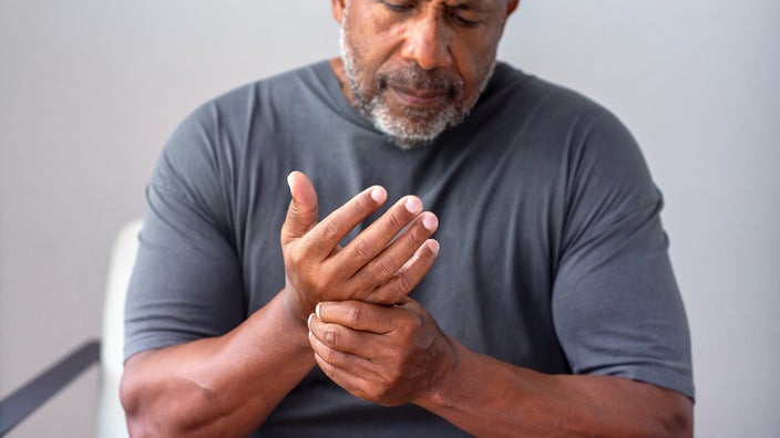Close-up cropped shot of a man rubbing his hands from arthritis pain. He is wearing a gray t-shirt.