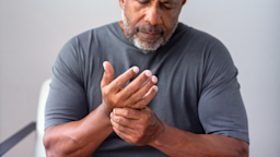 Close-up cropped shot of a man rubbing his hands from arthritis pain. He is wearing a gray t-shirt.
digitalskillet/iStock via Getty Images
