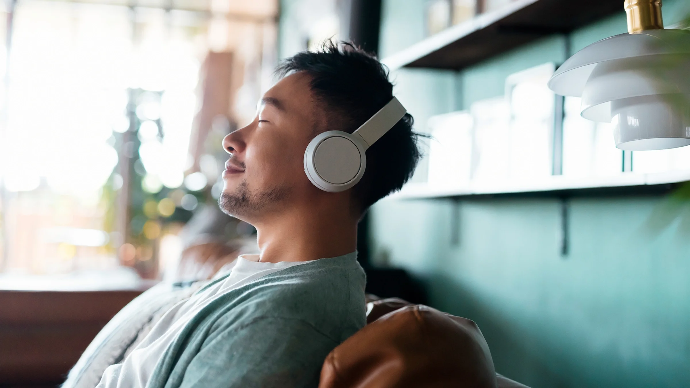 Man with eyes closed, enjoying music over headphones while relaxing on the sofa at home.