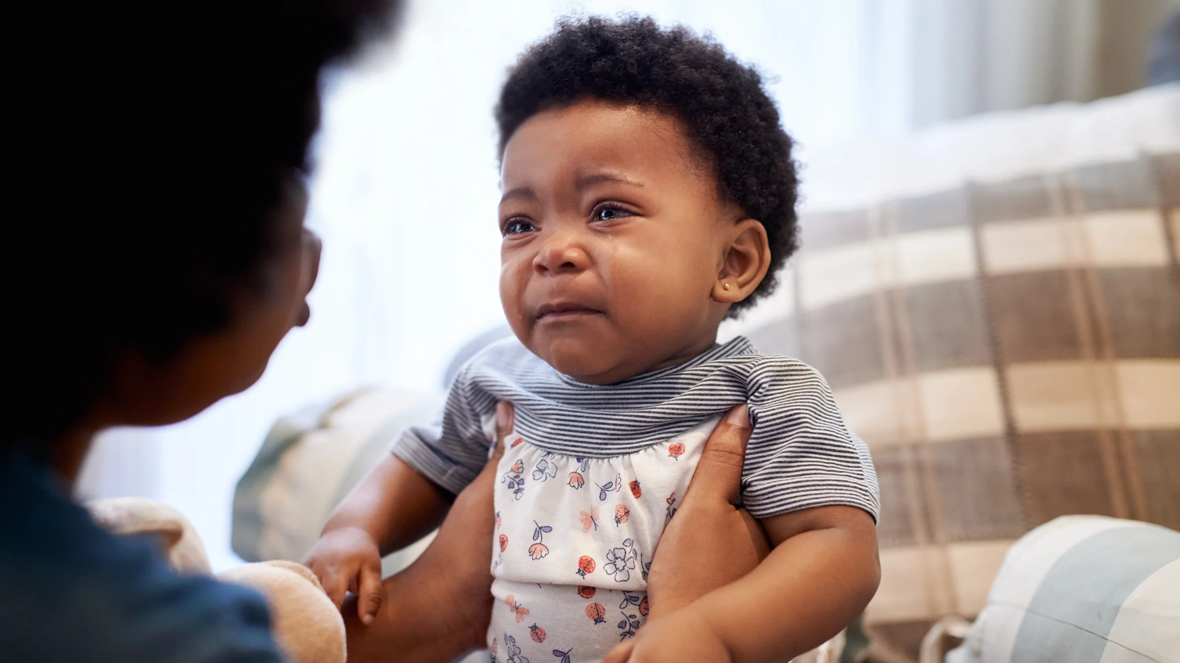 Pictured is a close-up view of a crying baby being held by their mother.