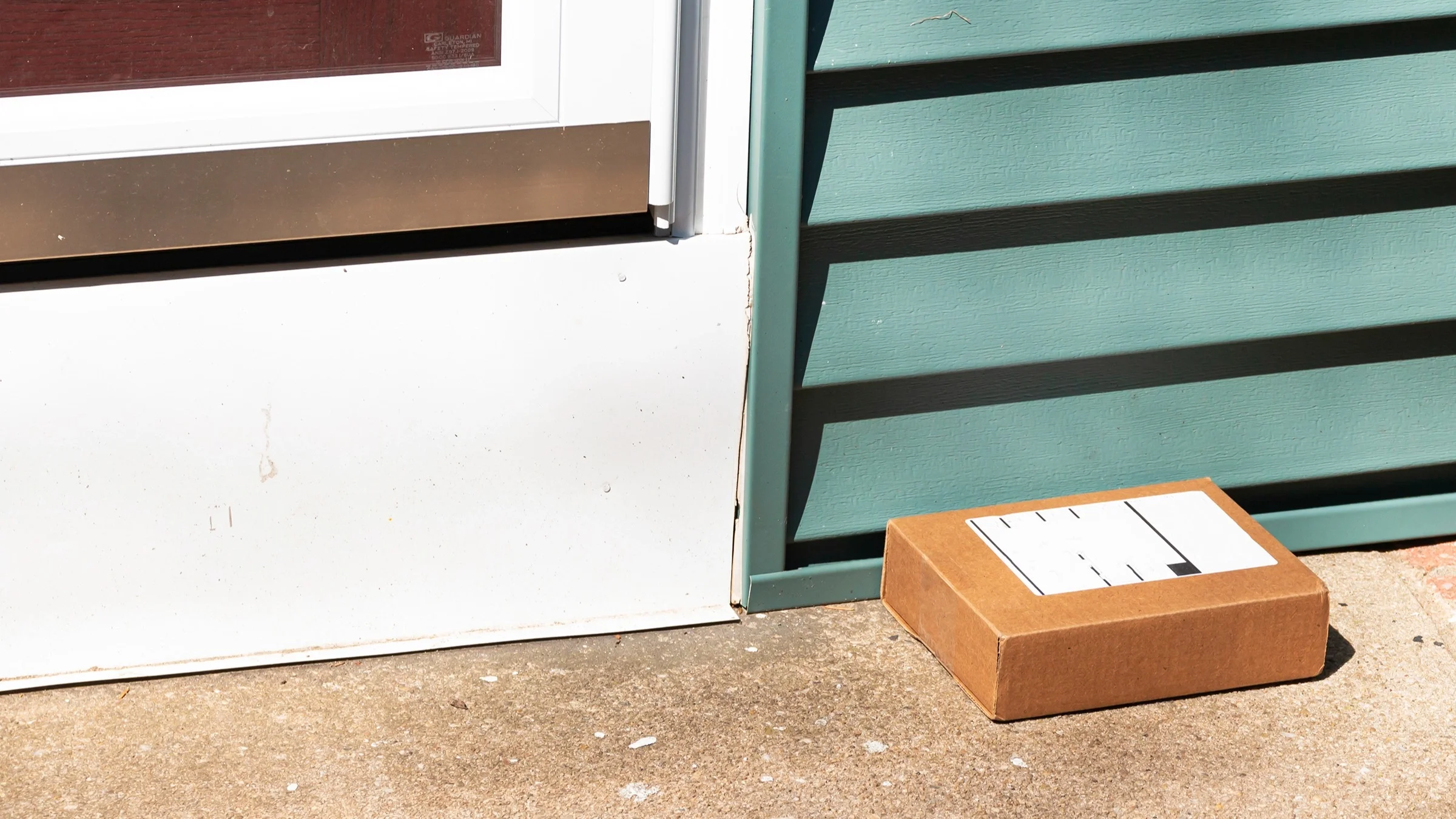 Small brown package on a doorstep in front of a teal colored house.