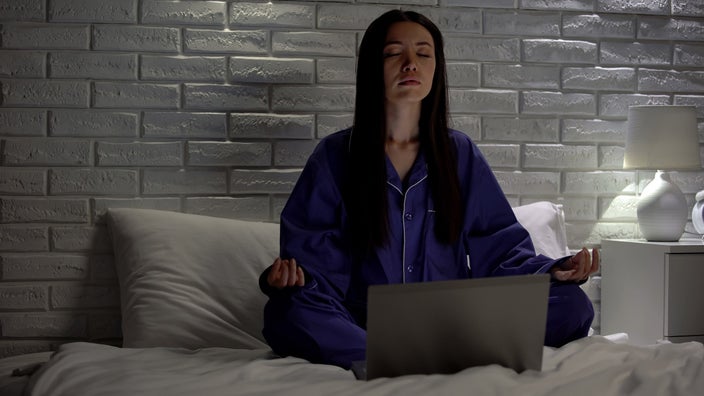 An older adult is meditating on her bed at home.