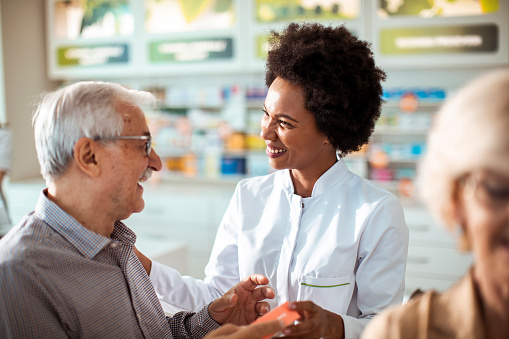 Pharmacist smiling and helping an elderly patient review medication at the drug store.