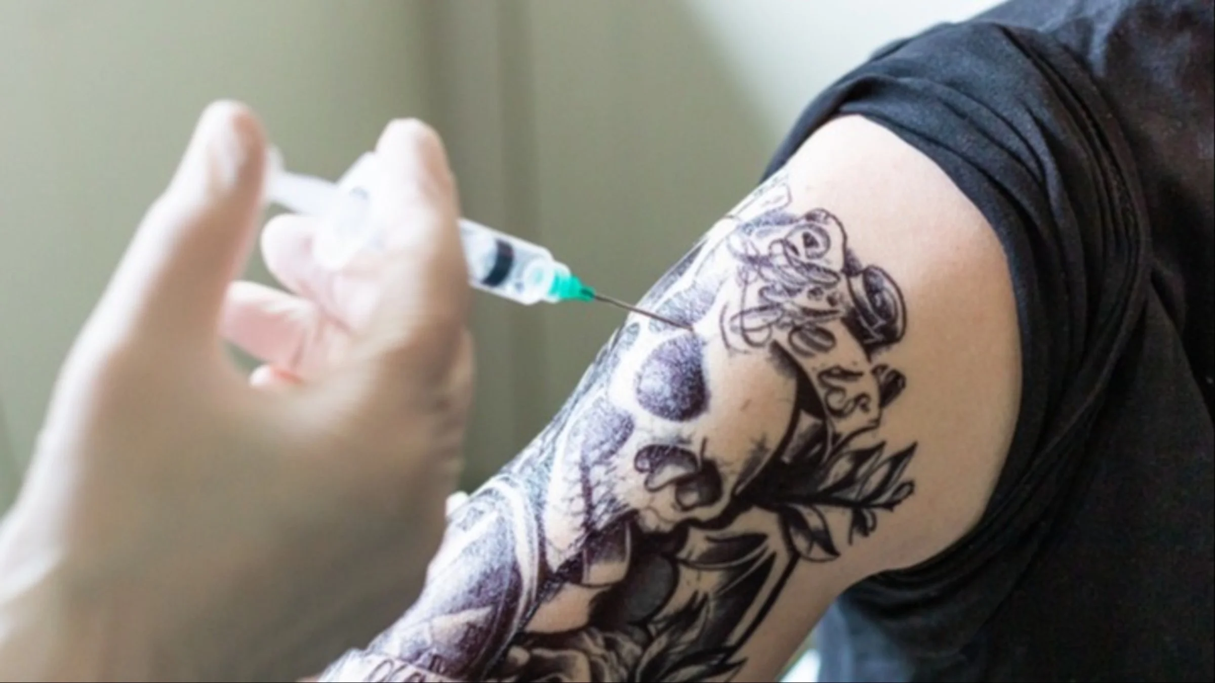 Close-up of a man with a tattooed arm getting an injection.