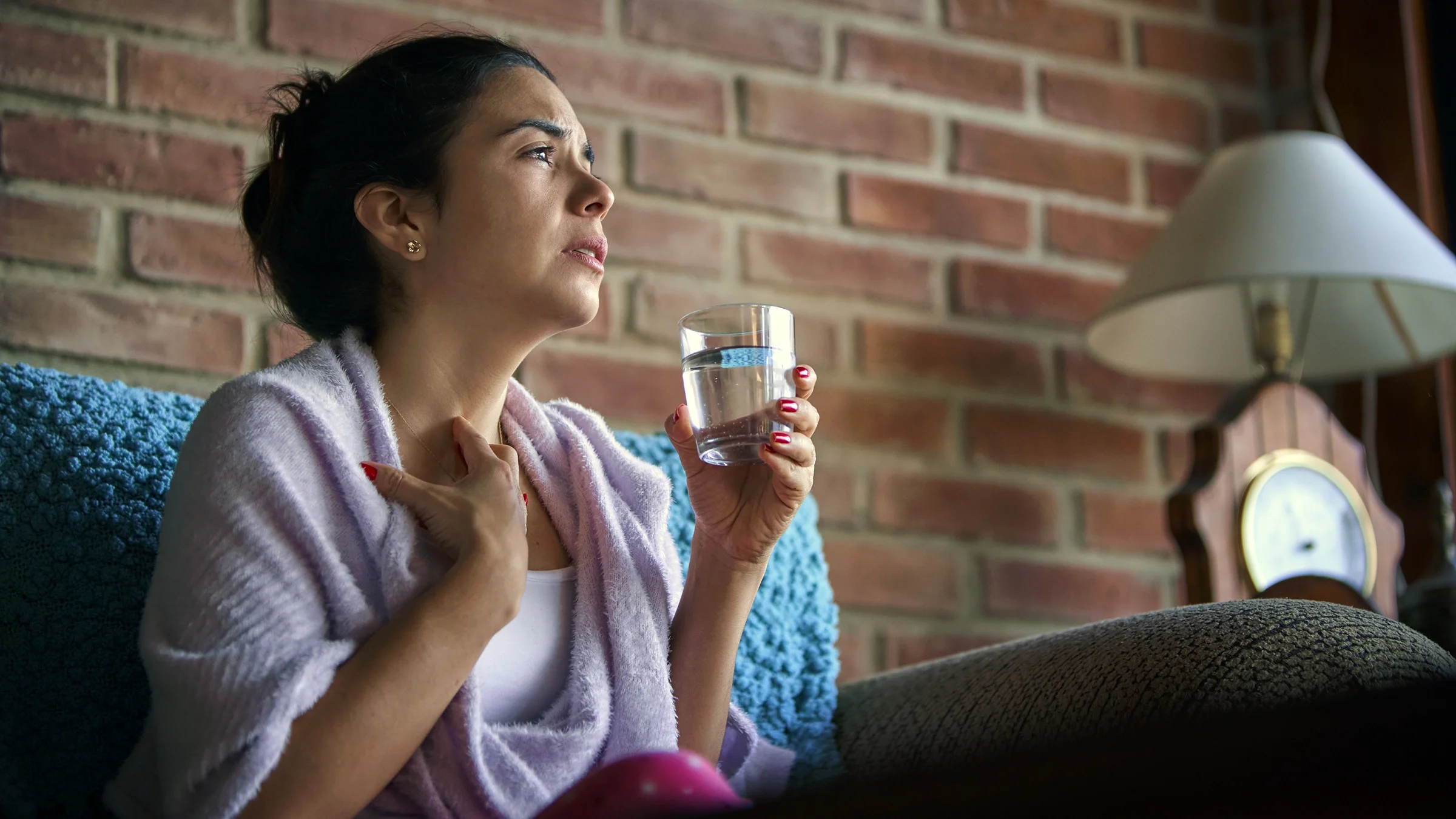 A person sitting on a couch puts hand to their throat.