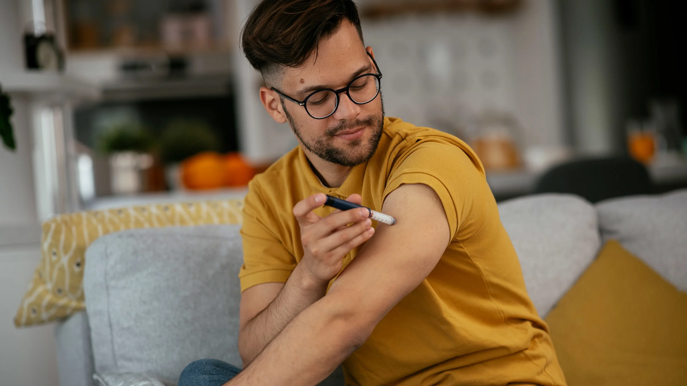 A person sitting on their couch and giving themself an insulin shot in their arm.