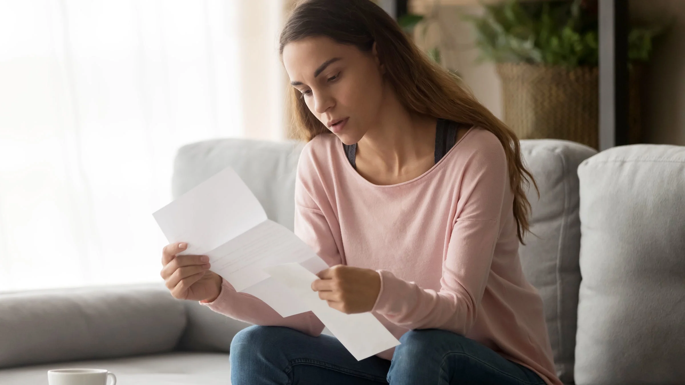 A woman carefully examines a document while sitting on the couch.